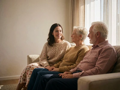 Older couple and a younger woman talking together on a sofa in a warm living room